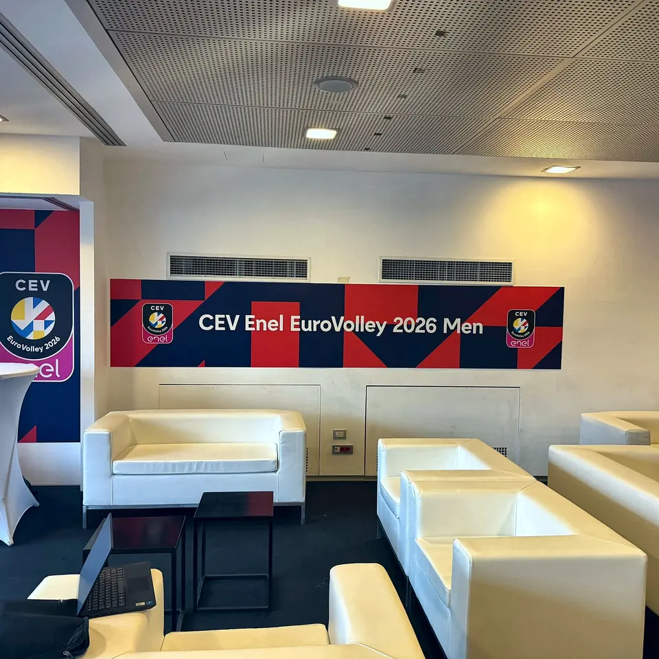 Area lounge di un evento sportivo con divanetti bianchi e pareti grafiche