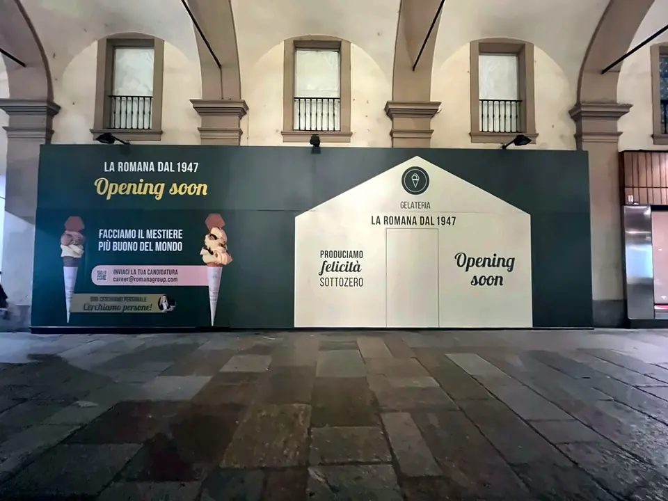Pannelli di cantiere stampati con la scritta Opening soon davanti a una vetrina sotto i portici