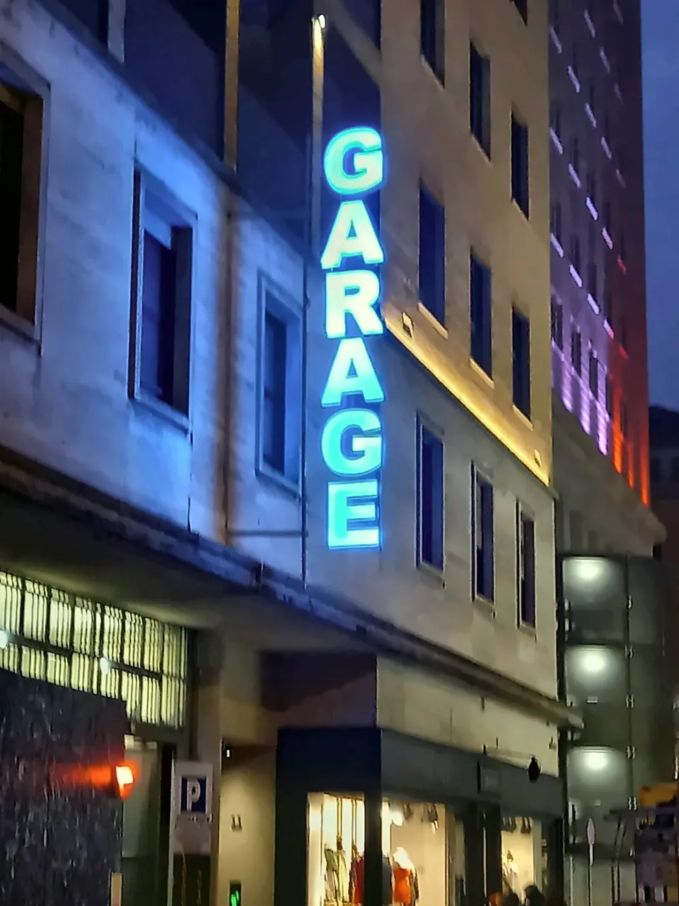 Insegna luminosa verticale accesa di sera sulla facciata di un garage