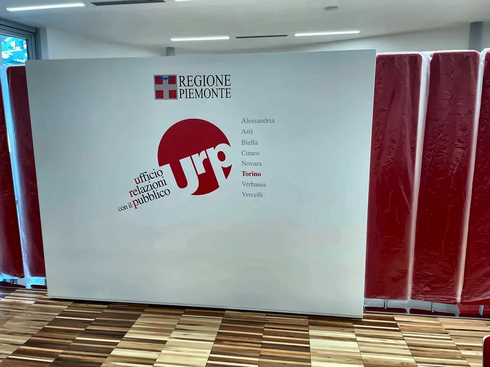 Parete grafica rossa e bianca con il logo di Regione Piemonte in un ufficio aperto al pubblico
