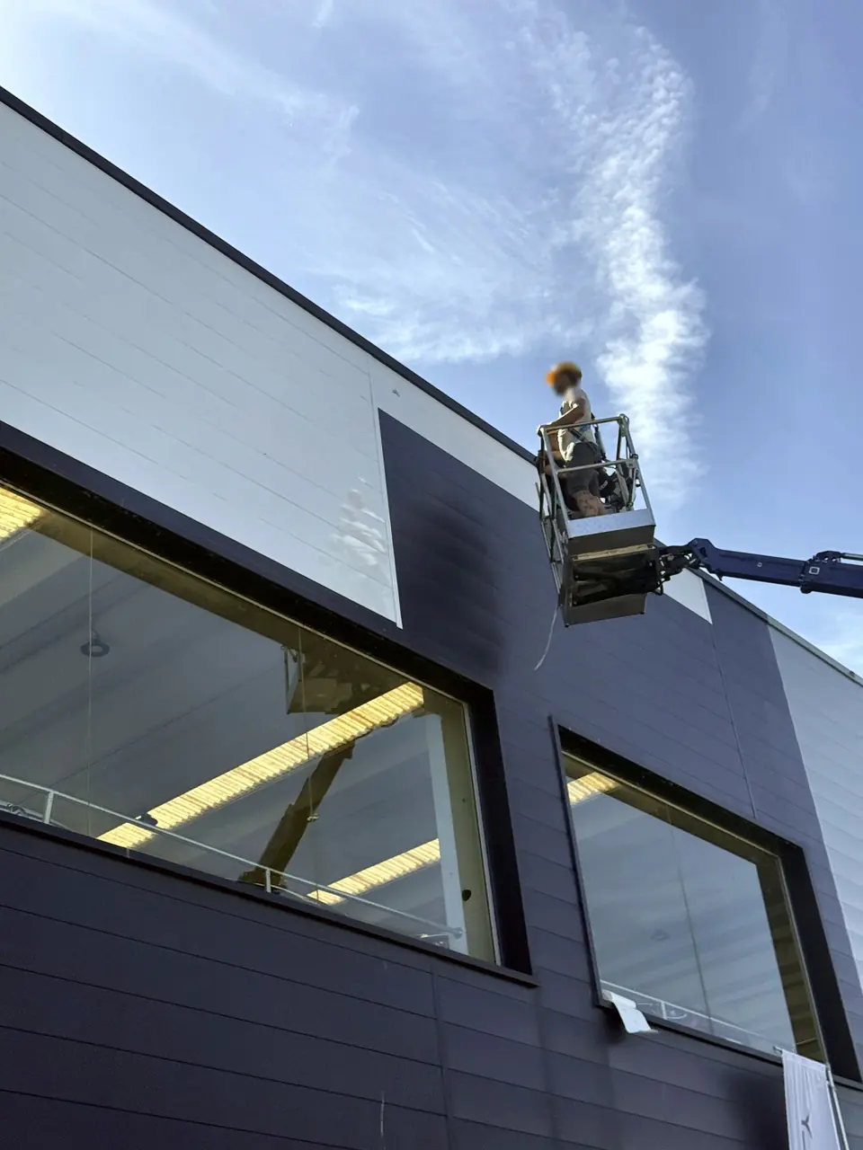 Installatore su un cestello elevatore al lavoro sulla facciata scura di un edificio moderno