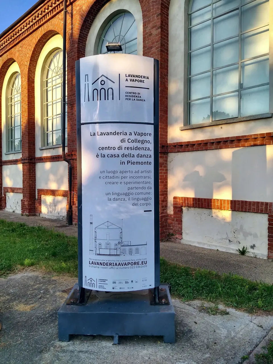 Totem informativo esterno davanti a un edificio storico in mattoni